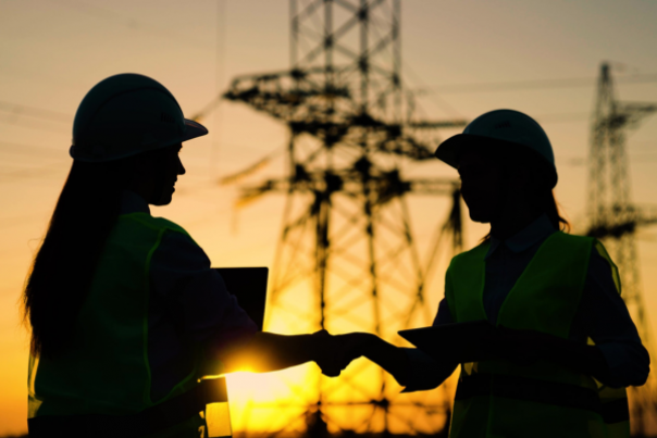 A silhouette of two workers shaking hands in front of transmission towers at sunset